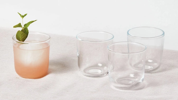 clear drinking glasses on a tablecloth, one is filled with juice and mint